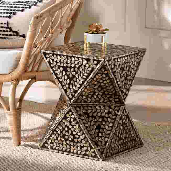 Modern bohemian end table with black and bronze mother of pearl inlay, placed next to a wicker chair.