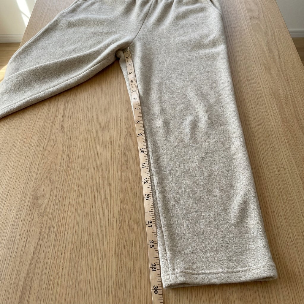 Folded knit pants with a soft tape measure laid along the inseam on a flat surface